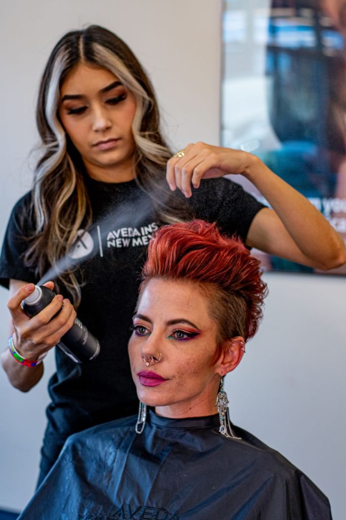 Woman spraying hair spray on styled woman's hair